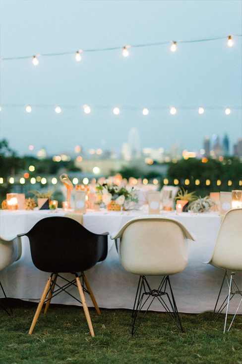 Black and white Eames molded plastic chairs and cafe lights at wedding reception overlooking downtown Dallas