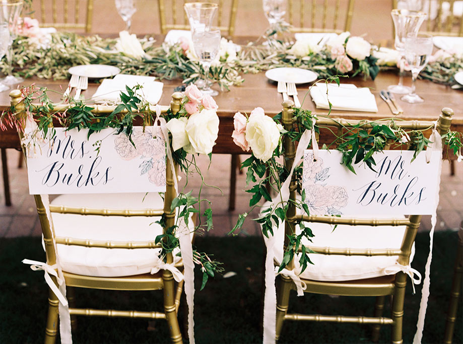 Wooden wedding reception head table with bride and groom calligraphy signs on gold chiavari chairs