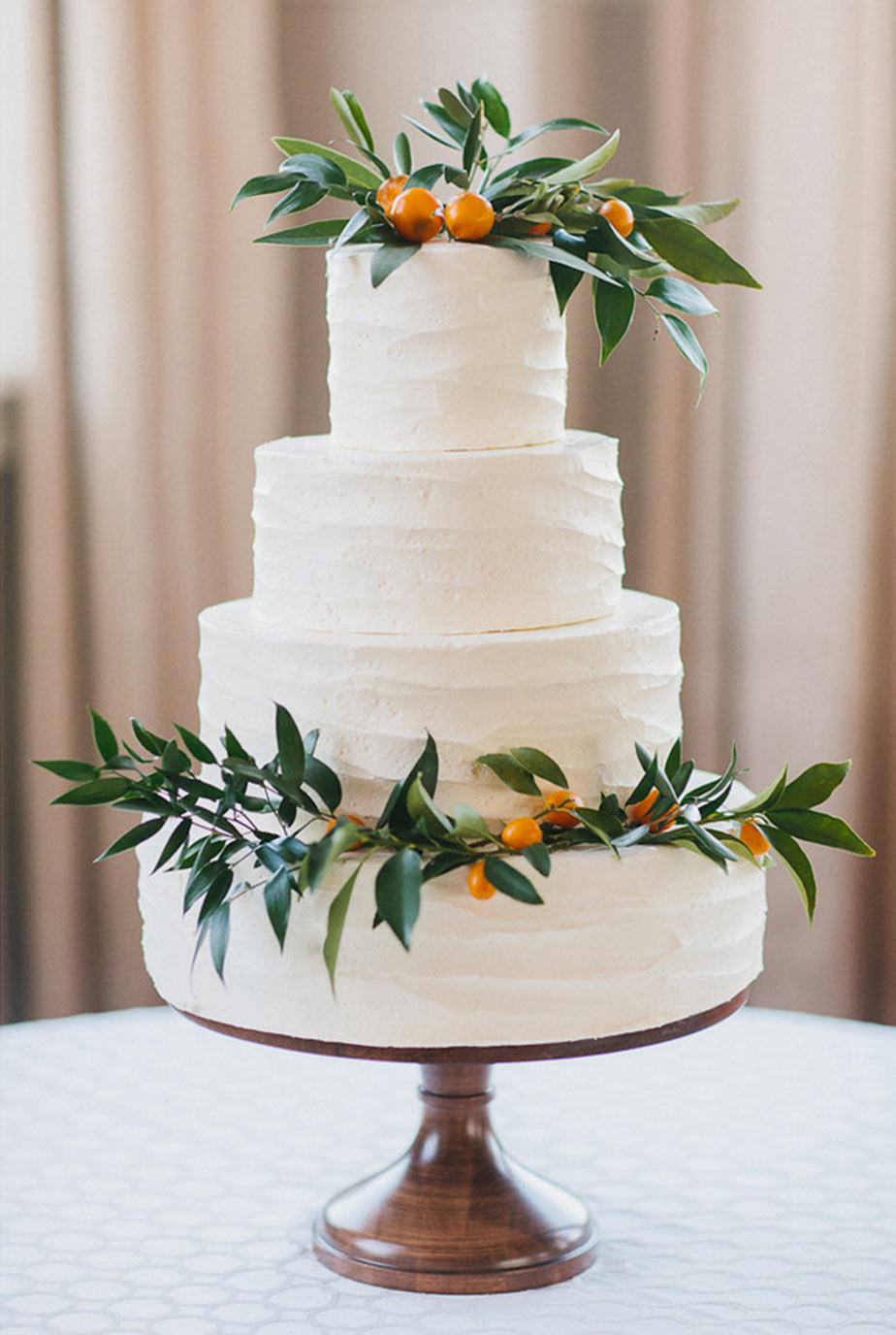 White buttercream wedding cake with floral greenery and kumquats