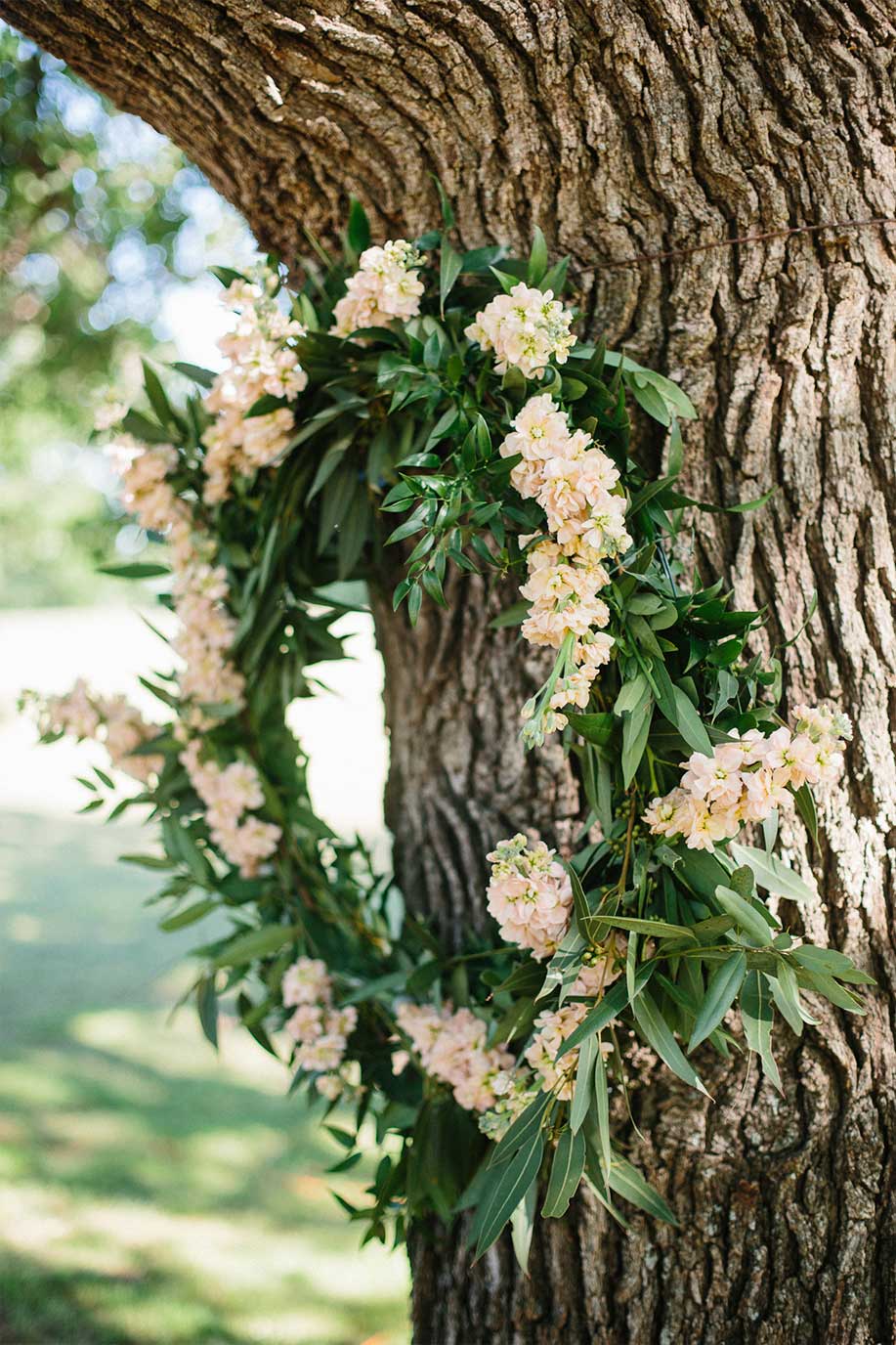 Peach floral and greenery wreath hanging on oak tree for outdoor wedding ceremony decor