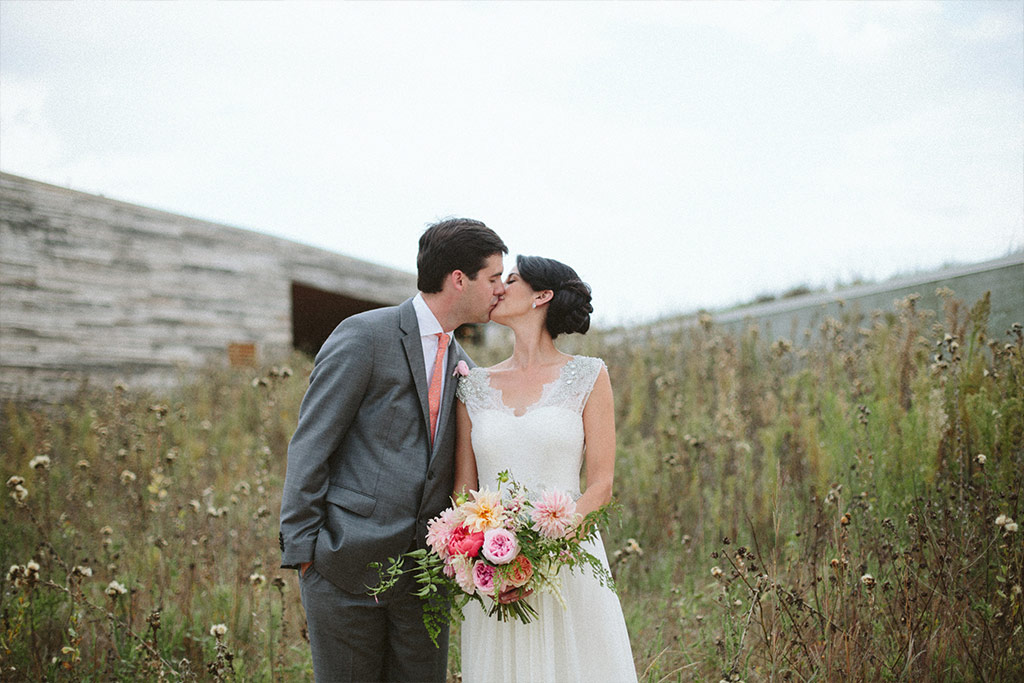 Bride and groom kiss for a wedding day portrait in front of Trinity River Audubon Center in Dallas