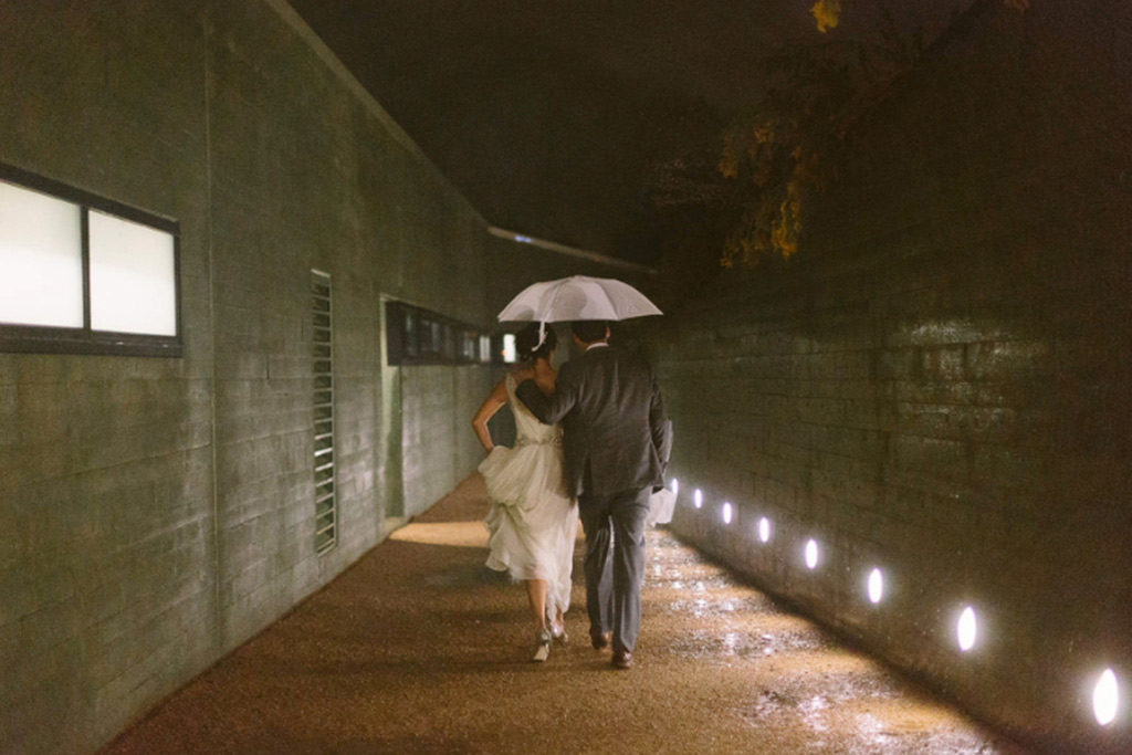Bride and groom leave wedding reception under umbrella in the rain