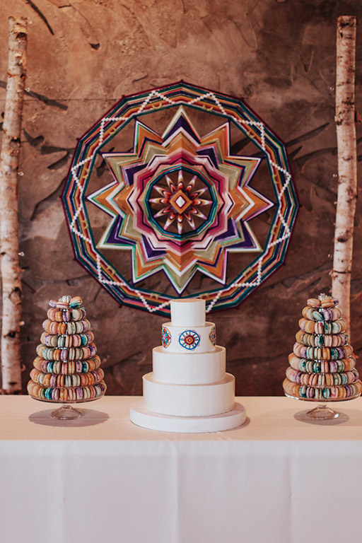 The wedding cake and macaroon towers, with a colorful, giant ojo de Dios or eye of God backdrop by Jay the Weaver