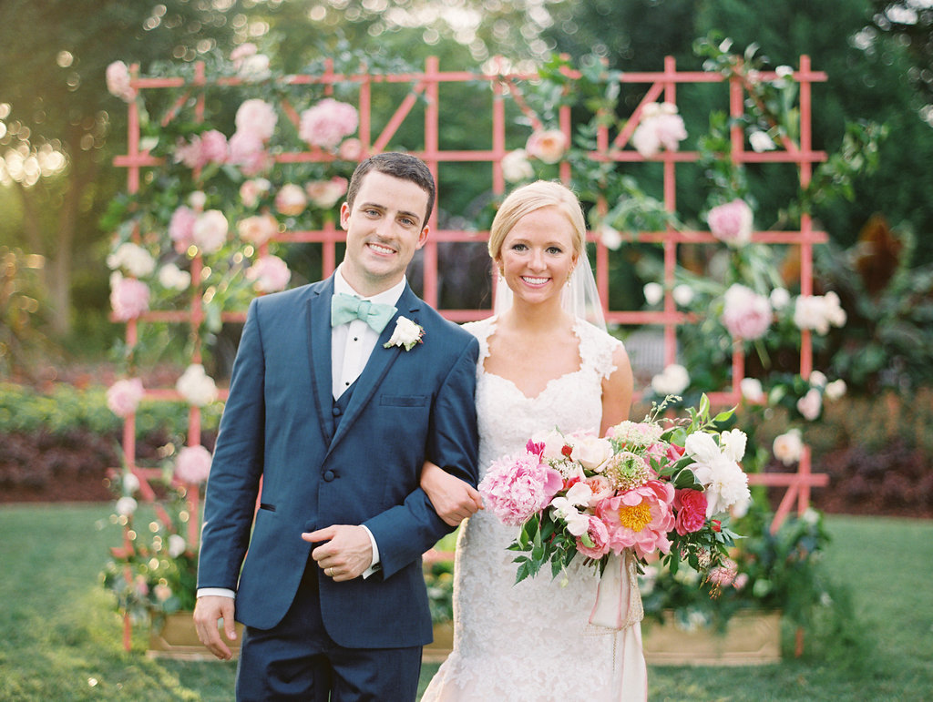 Bride and groom take a wedding day portrait in front of a pink floral lattice at The Dallas Arboretum