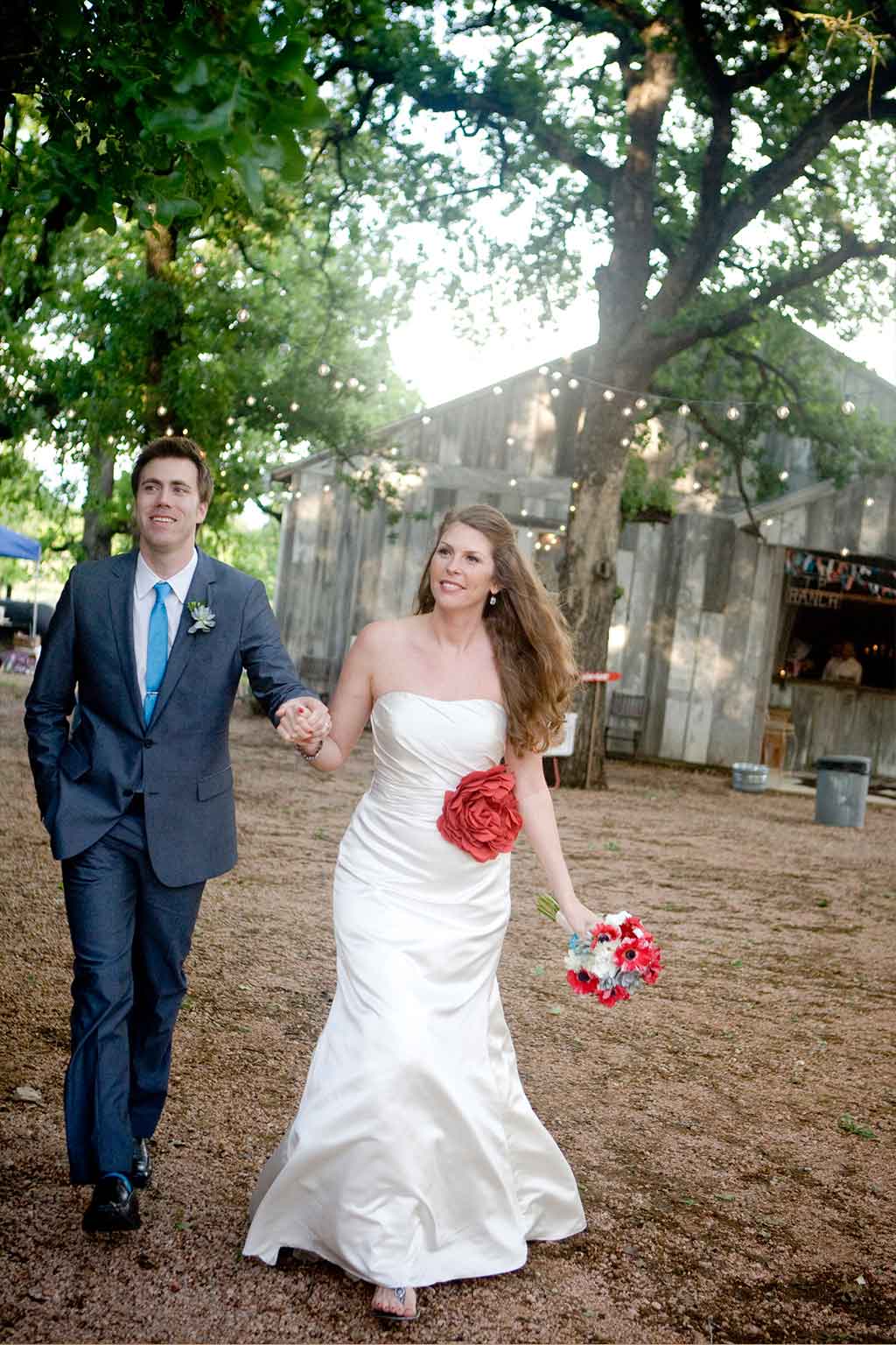 Bride and groom walking into wedding reception at Three Points Ranch in Texas Hill Country with barn and cafe lights