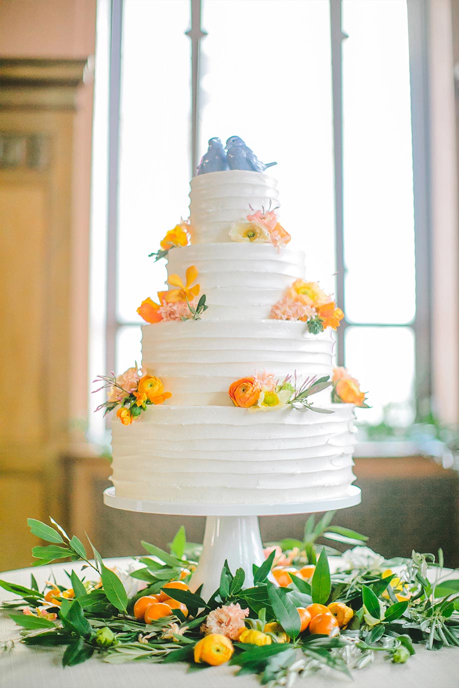 Buttercream wedding cake with orange and yellow flowers and blue and white porcelain topper