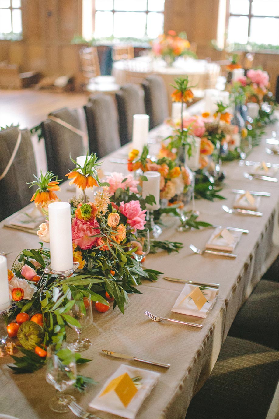 Long wedding head table with orange place cards, greenery and fruit garland