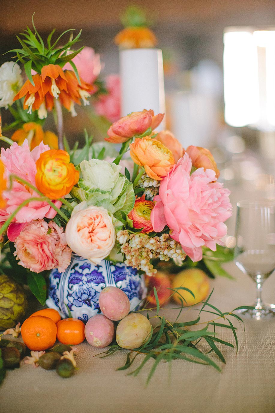 Pink and orange floral wedding centerpiece in blue and white porcelain vase with greenery and fruit