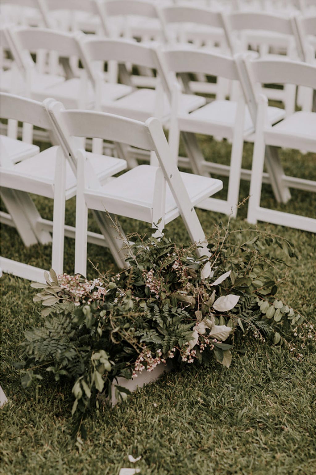 Natural green and white wedding aisle floral arrangement with white garden chairs