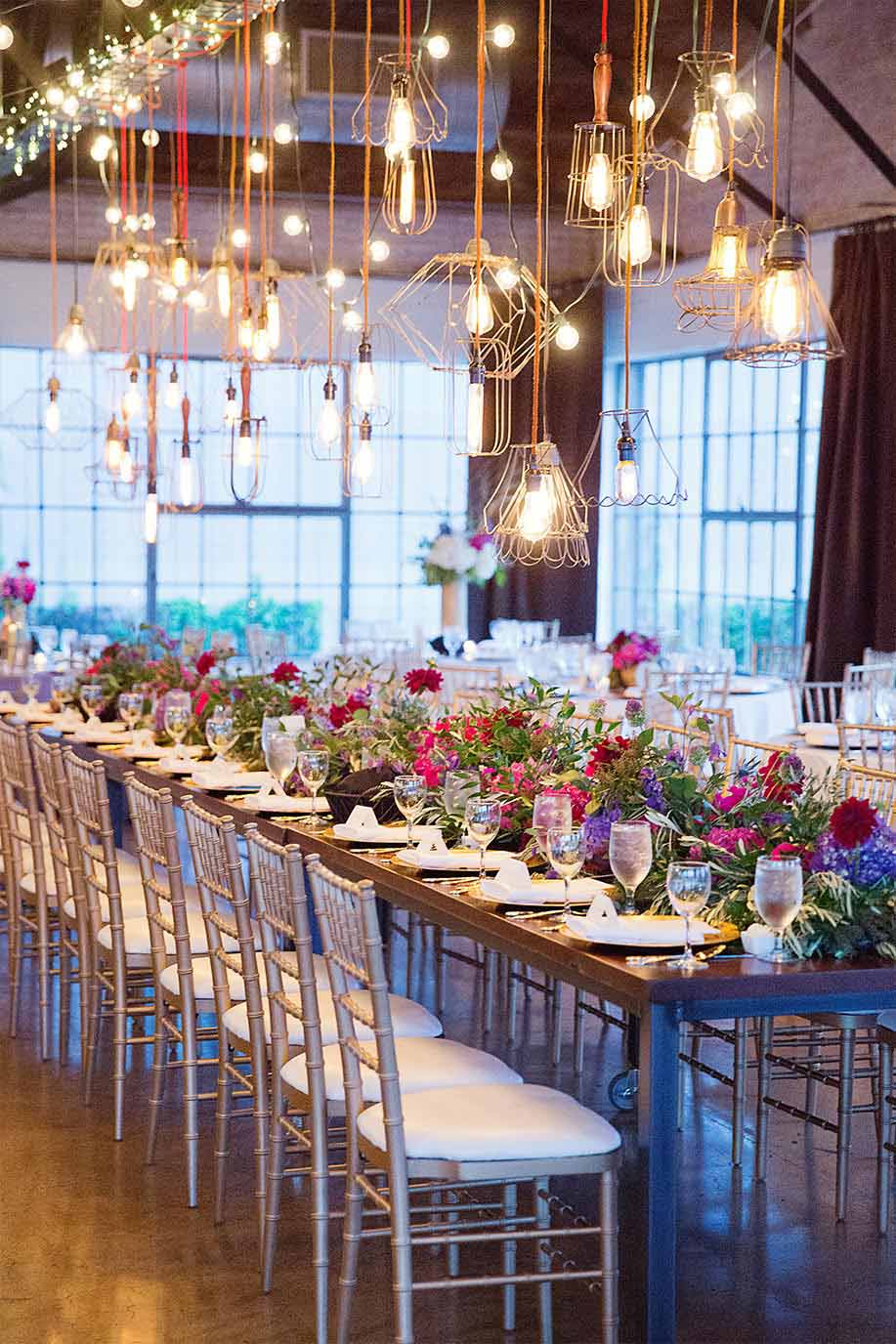 Wedding long head table with pink and purple floral garland and industrial cage lights at Hickory Street Annex in Dallas